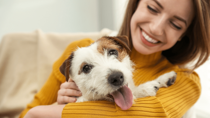 Image of a smiling woman cuddling her beloved pet, a cute jack russel terrier.